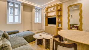 A modern living room with a sofa, a round table, a TV, and a wooden shelf unit. - A Sublim 1-BR Apartment - Saint Germain (Paris)