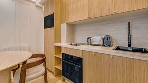 A compact kitchen with wooden cabinets, a built-in dishwasher, and a small countertop with a kettle and toaster. - A Sublim 1-BR Apartment - Saint Germain (Paris)