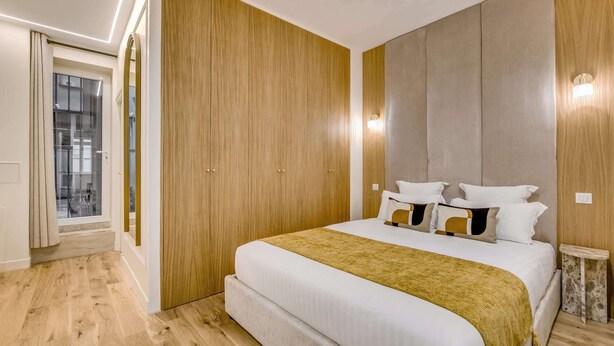 A bedroom with a large bed, wooden wardrobe, and a bedside table. - A Sublim 1-BR Apartment - Saint Germain (Paris)