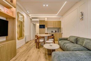 Ein modernes Wohnzimmer mit grauem Sofa, einem Holzespeisetisch und Stühlen, einem Fernseher und einer Küchenzeile mit Holdekor und einer Mikrowelle.
