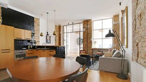 Moderni keittiö, jossa on puiset kaapit, pyöreä ruokapöytä ja tiiliseinä.