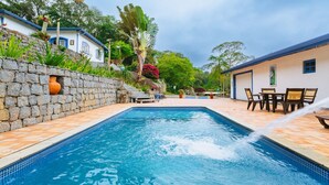 A swimming pool with a stone wall and a patio area with chairs and a table. - Country house with heated pool near São Paulo. (Mairiporã)