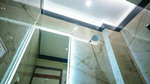 A modern bathroom with a glass-enclosed shower, marble walls, and a ceiling light fixture. - Sri Shyam Villas (VARANASI)