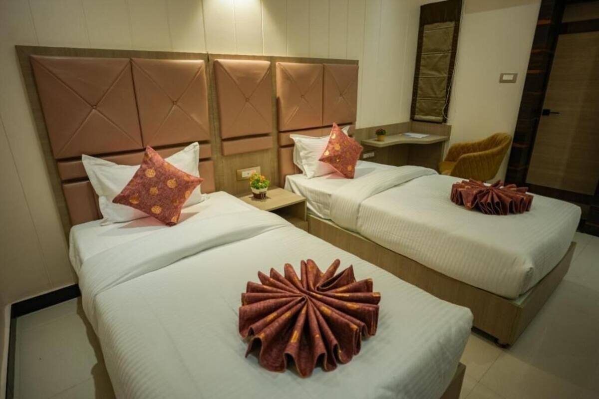Habitación de hotel con dos camas, cada una con cabecera, una mesita con una planta y una silla.