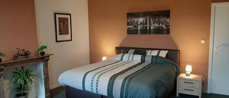 A bedroom with a bed, bedside tables, a nightstand, a fireplace, and a framed picture on the wall.