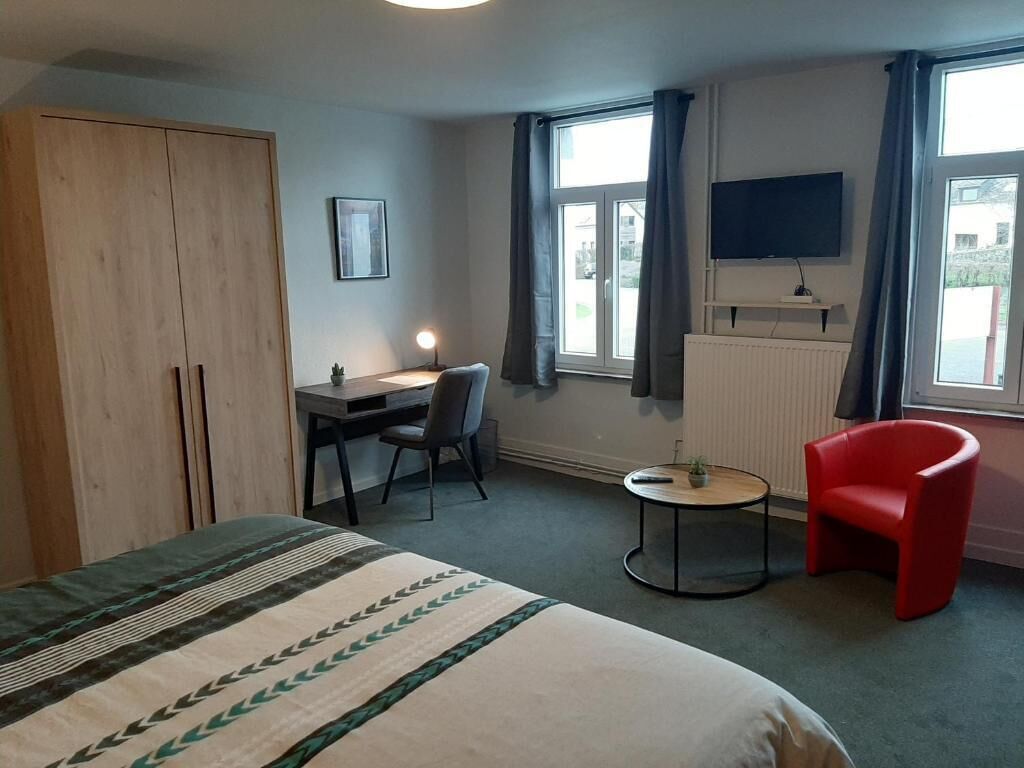 Een hotelkamer met een bed, een bureau met een stoel, een kleine tafel, een rode stoel en een aan de muur bevestigde televisie.