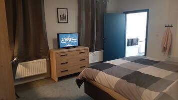 Une chambre à coucher avec un lit, une commode, un téléviseur, une porte et une fenêtre.