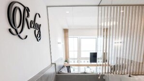 A modern bathroom with a large bathtub, a glass partition, and a view of a living area with a sofa and a TV. - Porto Sea View - Luxury Junior Suites (Thessaloniki)