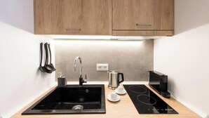 A modern kitchen with a black sink, stainless steel faucet, wooden cabinets, a kettle, a coffee maker, and a built-in induction cooktop. - Porto Sea View - Luxury Junior Suites (Thessaloniki)