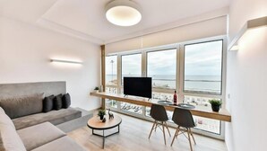 A modern living room with a large window, a flat-screen TV, a sofa, a coffee table, and two chairs. - Porto Sea View - Luxury Junior Suites (Thessaloniki)