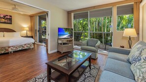 A hotel room with a bed, a TV, a sofa, and a large window with a view of palm trees. - Maui Banyan Kihei condo w/ lanai and resort pool, summer deal (Kihei)