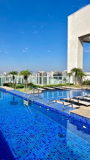 Una piscina sul tetto con piastrelle blu cristalline, circondata da palme e edifici moderni.