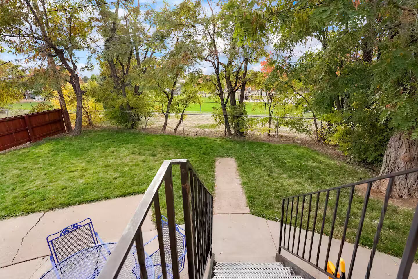 A backyard with a grassy lawn, a metal staircase, and a metal chair.