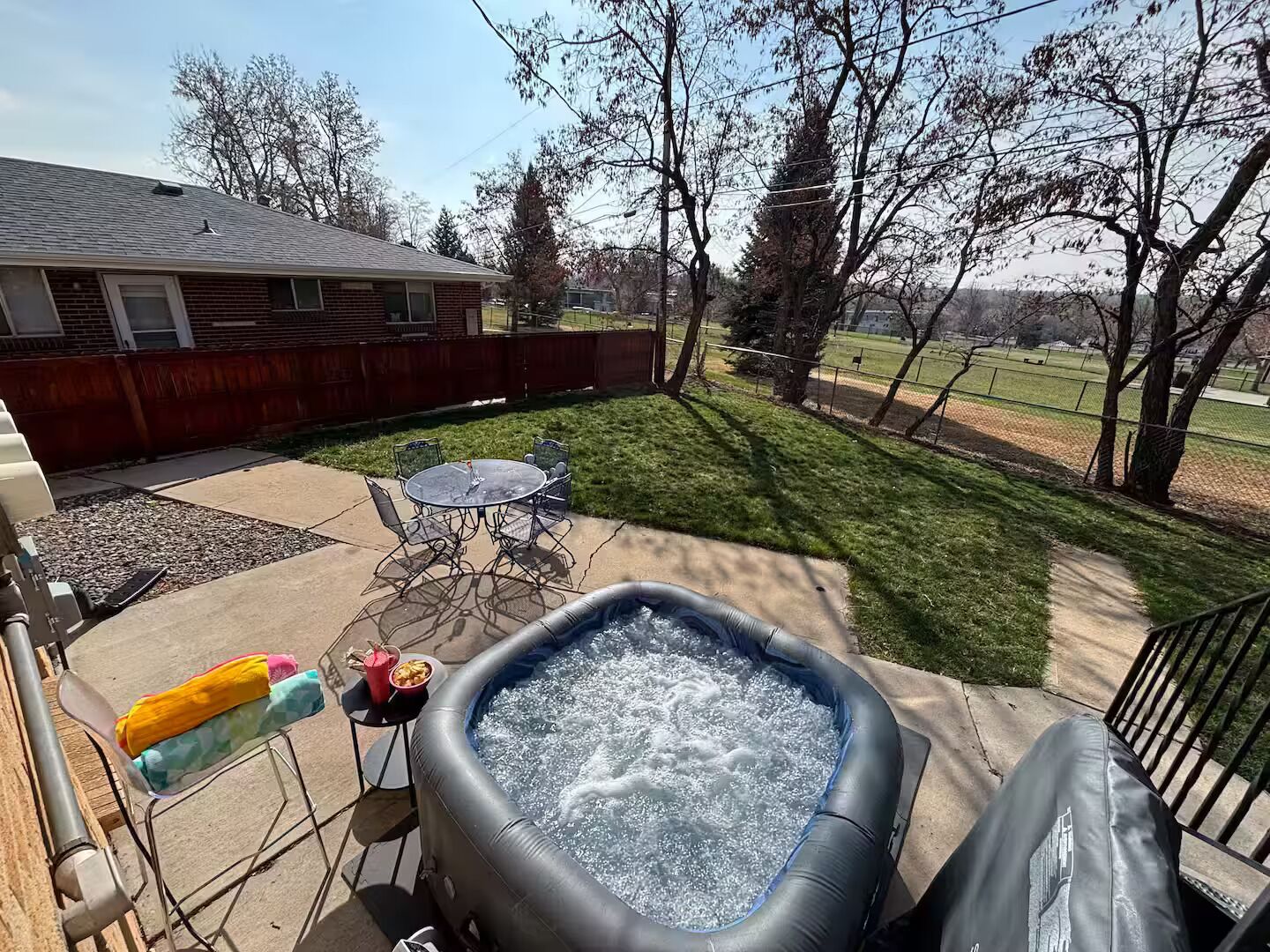 An outdoor patio with a hot tub, a table with chairs, and a small inflatable pool.