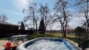 Un jacuzzi gonflable installé dans un jardin, avec une table et des chaises, entouré d’arbres et d’une clôture.