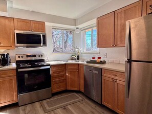 A modern kitchen with wooden cabinets, stainless steel appliances, and a window with a view of trees. - Park side, Pets, 420, Hot Tub, Quiet, 1Gb Internet (Arvada)