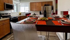 Une cuisine moderne avec des meubles en bois, un réfrigérateur en acier inoxydable, un four à micro-ondes et un coin repas avec une table dressée pour deux personnes.