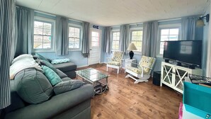 Een woonkamer met een bank, fauteuils, een salontafel, een televisie en een boekenkast.