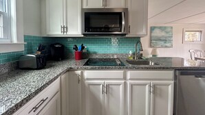Een keuken met witte kastjes, een roestvrijstalen magnetron, een rode beker met bestek, en een blauwgroene achterwand.