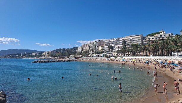 A beach with clear blue water, people swimming and sunbathing, and buildings in the background. - Family apartment with swimming pool and sea view, quietly located with parking. (Cannes)