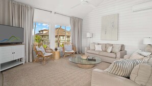 A spacious living room with a large TV, wicker chairs, a beige sofa, and a glass coffee table. - Regency at Poipu Kai 123 By Parrish Kauai - Short walk to Beach (Koloa)