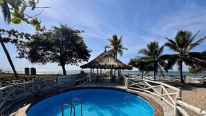 Un área de piscina con muelle de madera, una escalera y una estructura cubierta de paja.