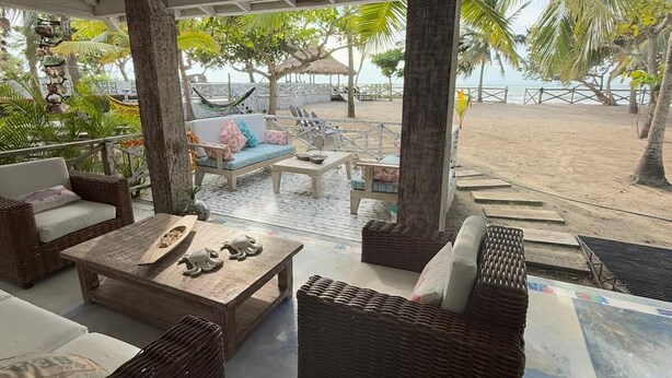 Un área de descanso al aire libre con muebles de mimbre, una mesa de centro de madera y vista a la playa.