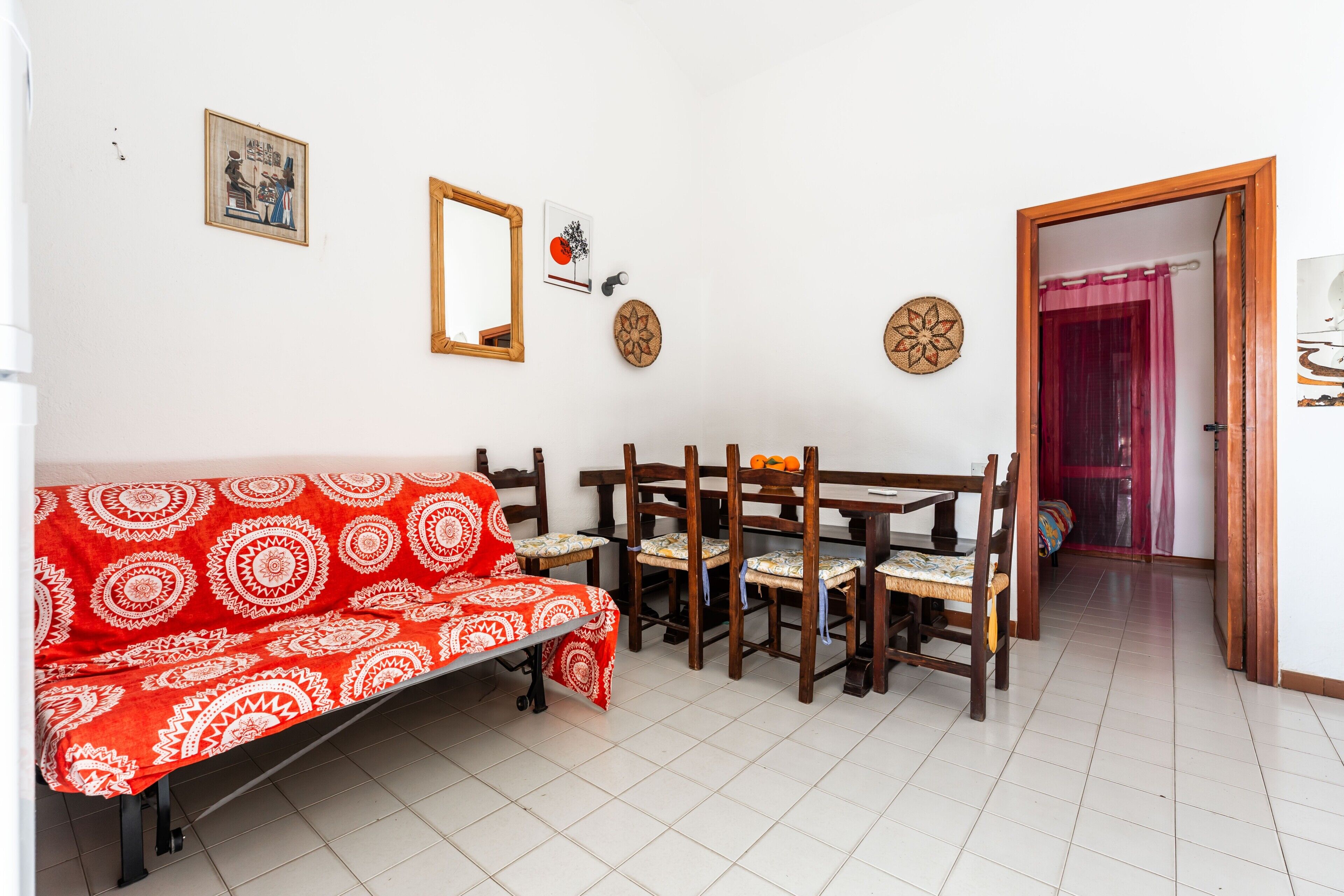 A room with a red patterned sofa, wooden dining table with chairs, a mirror, and wall decorations.