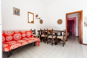 A room with a red patterned sofa, wooden dining table with chairs, a mirror, and wall decorations.