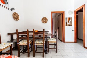 A dining area with a wooden table and chairs, a white tiled floor, and a door leading to another room.