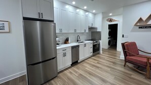 A modern kitchen with white cabinets, stainless steel appliances, and a wooden floor. - Brand New Modern Mountain Suite w/heated driveway and sidewalks (Revelstoke)