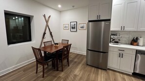A modern kitchen with white cabinets, a stainless steel refrigerator, wooden dining table, and chairs. - Brand New Modern Mountain Suite w/heated driveway and sidewalks (Revelstoke)