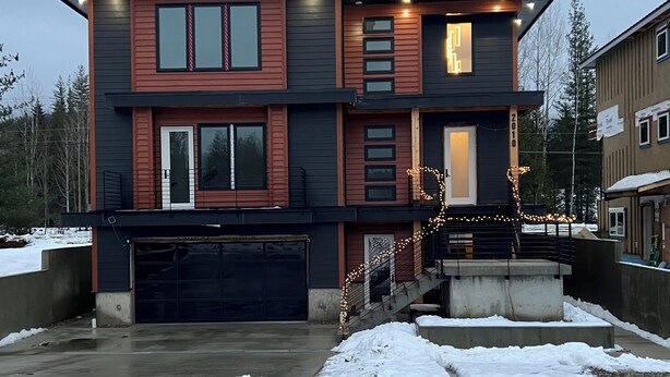 A modern two-story house with a garage, a covered outdoor area, and a staircase leading to the upper floor. - Brand New Modern Mountain Suite w/heated driveway and sidewalks (Revelstoke)
