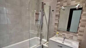 Ett modernt badrum med en dusch som är avskärmad med glasväggar, ett vitt handfat och en stor spegel.