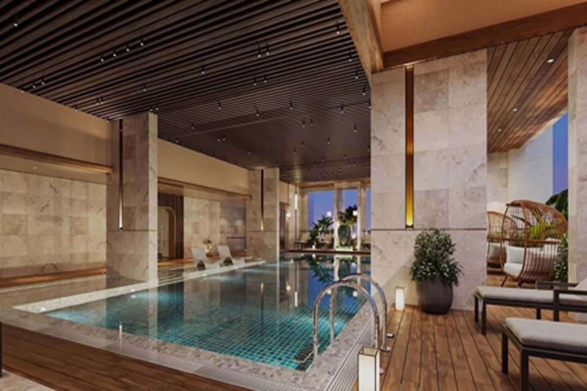 A modern indoor swimming pool with a wooden deck, stone walls, and a ceiling with linear lighting.