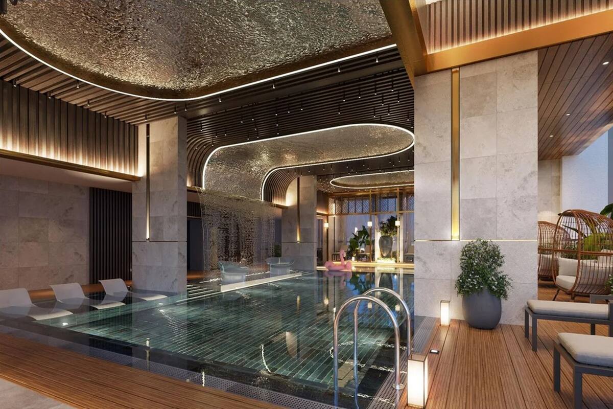 A modern indoor pool area with a glass barrier, wooden deck, and seating areas.