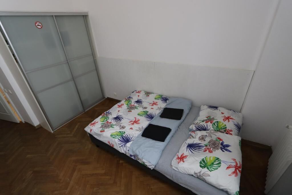 A small, single-bed room with a wooden floor, a bed with floral bedding, and a sliding door with a 'no smoking' sign.