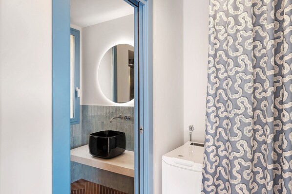 Une salle de bain avec un lavabo noir, un miroir rond et un évier blanc.