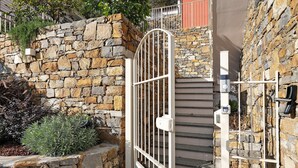 Un muro de piedra con una reja metálica, una escalera y un pequeño jardín.