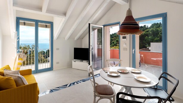 A modern living room with a sofa, dining table, chairs, a TV, and a balcony with a view. - Apartment 'Verde Mare' with Sea View, Private Terrace and Wi-Fi (Andora)