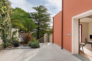 A building with a red exterior, a gated entrance, and a small patio area with plants and a seating area. - Apartment 'Corallo' with Sea View, Private Terrace and Wi-Fi (Andora)