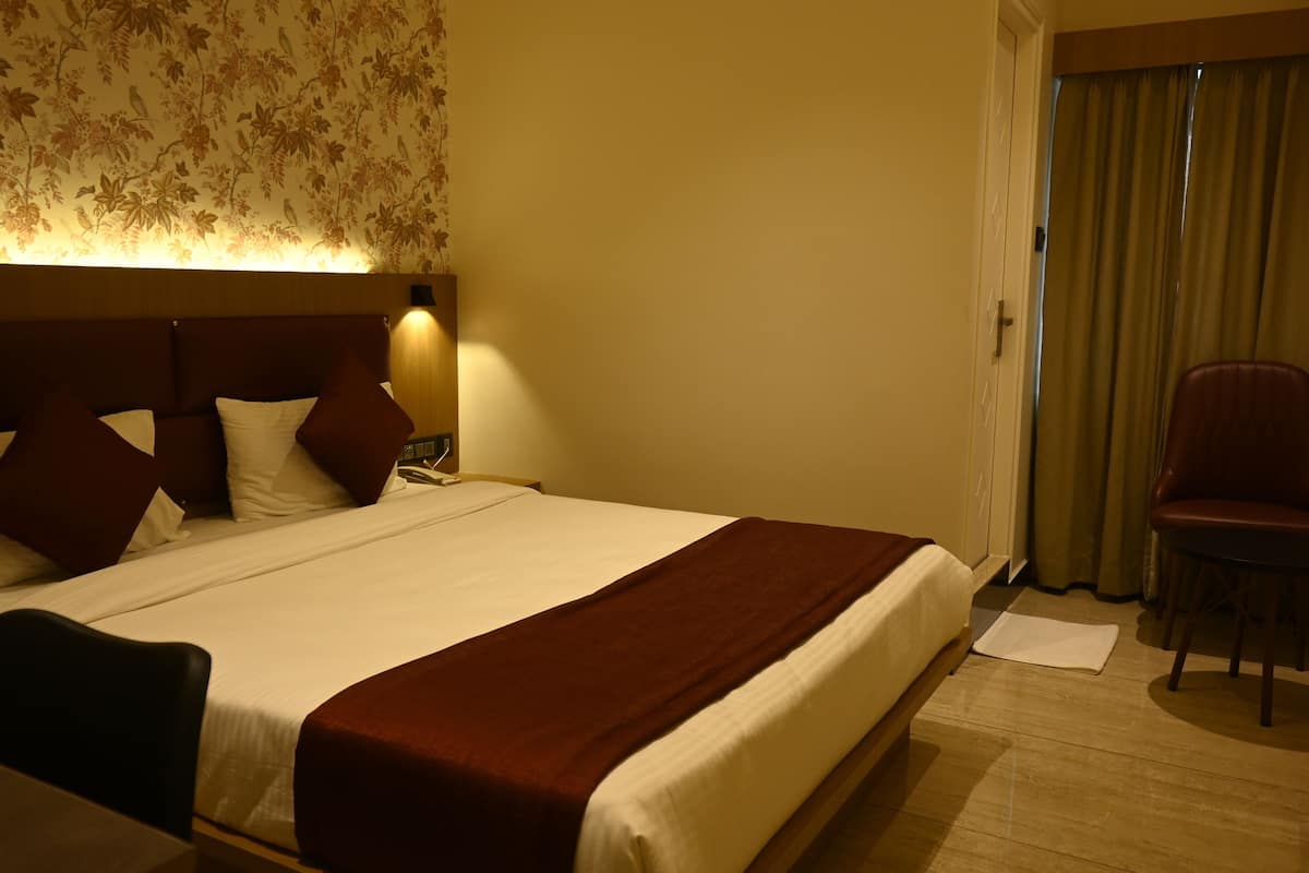 A hotel room with a large bed, a nightstand, a lamp, a chair, and a window with curtains.