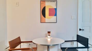 A room with a round table and two chairs, one brown and one black. A colorful poster is on the wall.