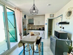Een compacte keuken met een eethoek, een televisie en een schuifdeur naar een balkon.