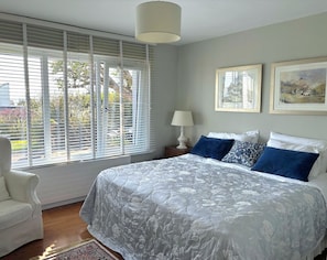 A bedroom with a large bed, a nightstand, a chair, and a window with blinds.