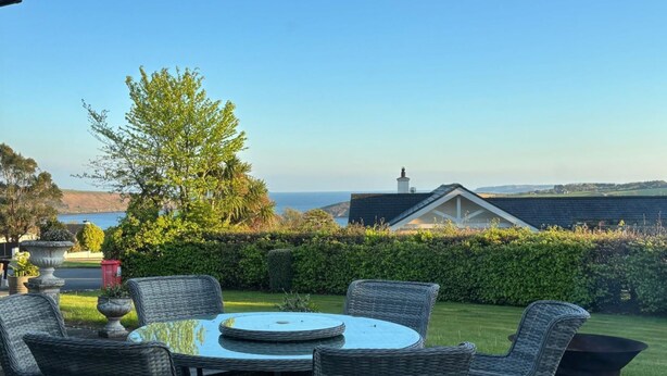 Une terrasse dotée de meubles en osier, d’une table ronde et offrant une vue sur la mer et les collines.
