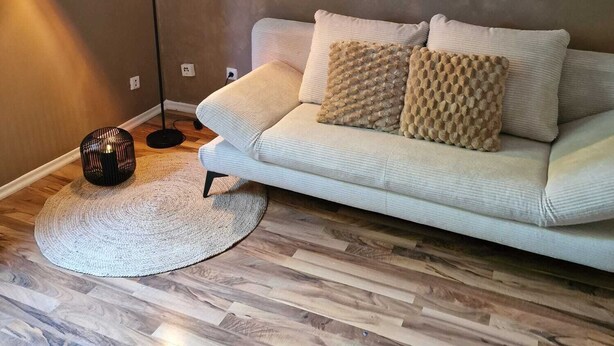 Ein Wohnzimmer mit einem weißen Sofa, zwei strukturierten Kissen, einer Stehlampe, einem gewebten Teppich und Holzböden.