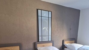 Ein Hotelzimmer mit zwei Einzelbetten, jeweils mit weißer Bettwäsche und Kissen, einem kleinen Nachttisch mit Lampe sowie einem großen Spiegel an der Wand.