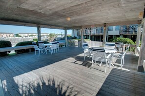 A covered outdoor area with wooden flooring, white plastic chairs, and tables. - Oceanview 2BR Condo w/ Pool, Easy Beach Access, Private Deck & Relaxing Escape (Emerald Isle)