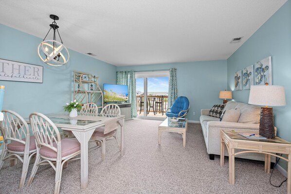 A living room with a glass table, wicker chairs, a sofa, and a lamp. - Oceanview 2BR Condo w/ Pool, Easy Beach Access, Private Deck & Relaxing Escape (Emerald Isle)
